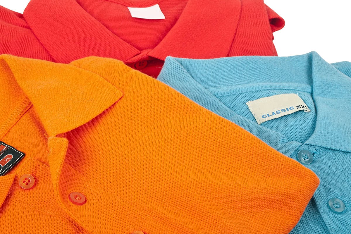 Colorful Polos A close-up image of three polo shirts in vibrant colors: red, orange, and light blue, showcasing their collars and buttons. The labels indicate sizes and styles.